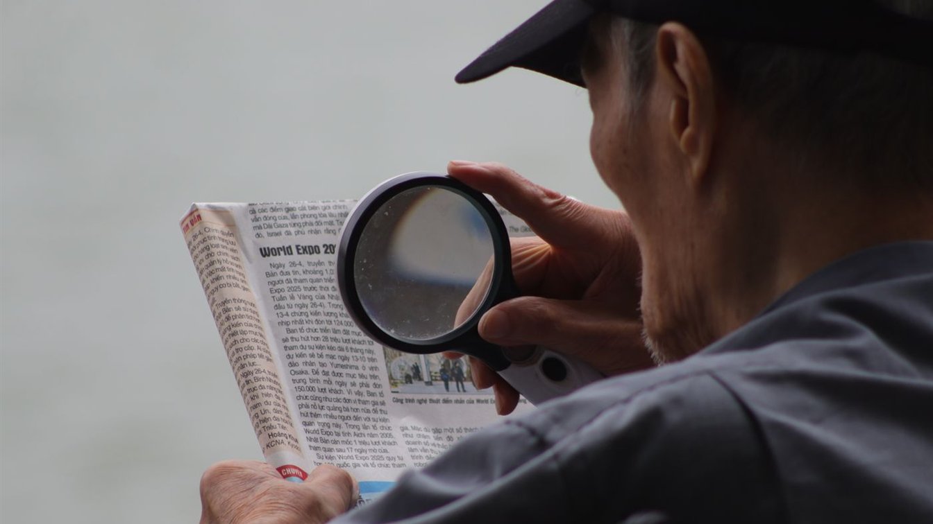 A reader studying a newspaper through a magnifying glass